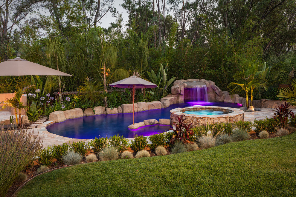 Exotisk inredning av en stor njurformad pool på baksidan av huset, med naturstensplattor och en fontän
