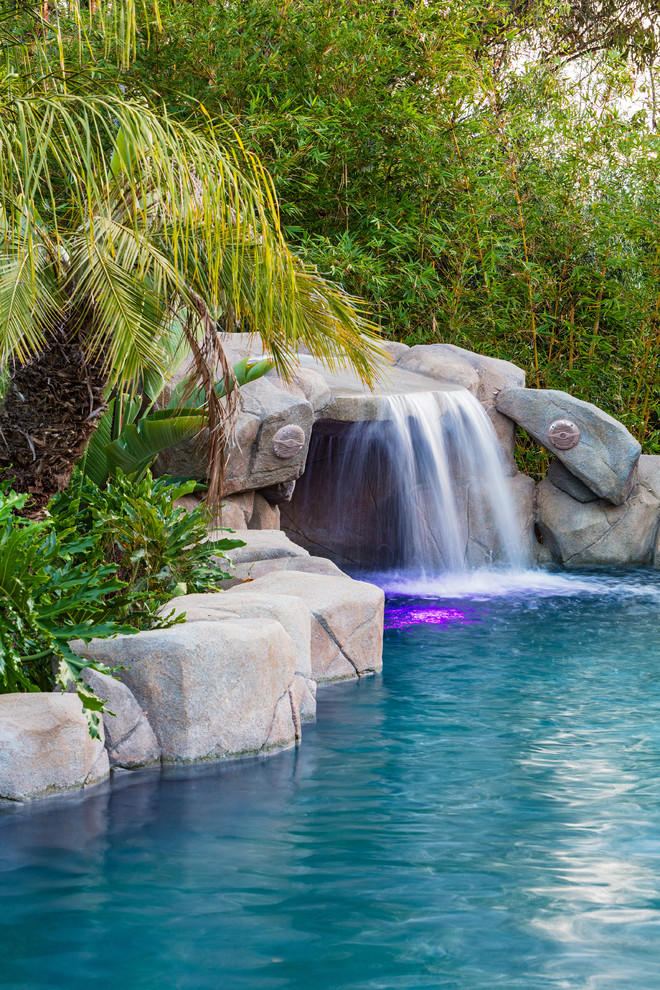 Idée de décoration pour une grande piscine naturelle et arrière ethnique sur mesure avec des pavés en pierre naturelle.