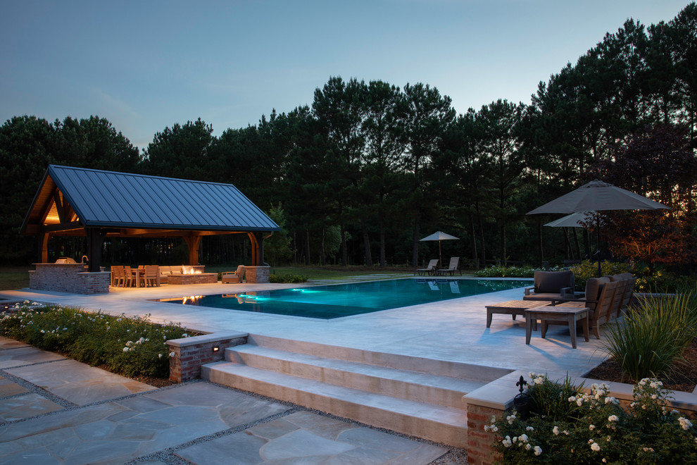 This is an example of a large traditional back rectangular infinity swimming pool in Dallas with a pool house and natural stone paving.