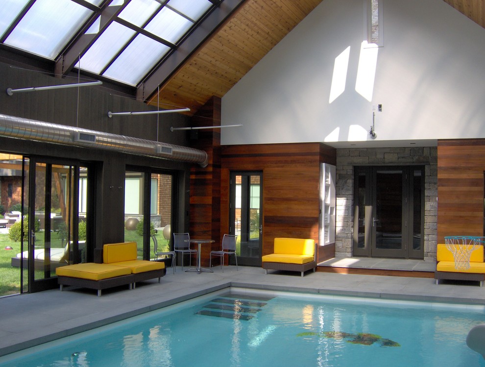 Photo of a large contemporary indoor rectangular swimming pool in New York with a pool house and concrete slabs.