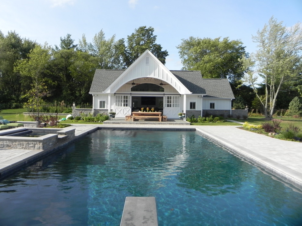 Exempel på en lantlig l-formad pool på baksidan av huset, med poolhus och naturstensplattor