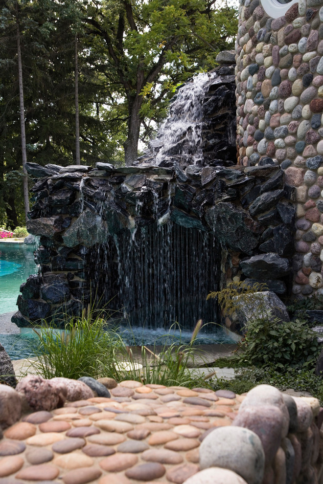 На фото: огромный бассейн-инфинити произвольной формы на заднем дворе в средиземноморском стиле с покрытием из каменной брусчатки и джакузи