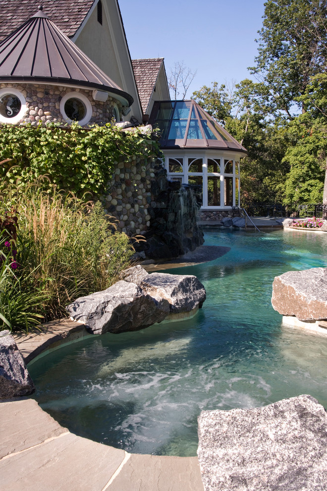 Foto di un'ampia piscina a sfioro infinito mediterranea personalizzata dietro casa con pavimentazioni in pietra naturale e una vasca idromassaggio