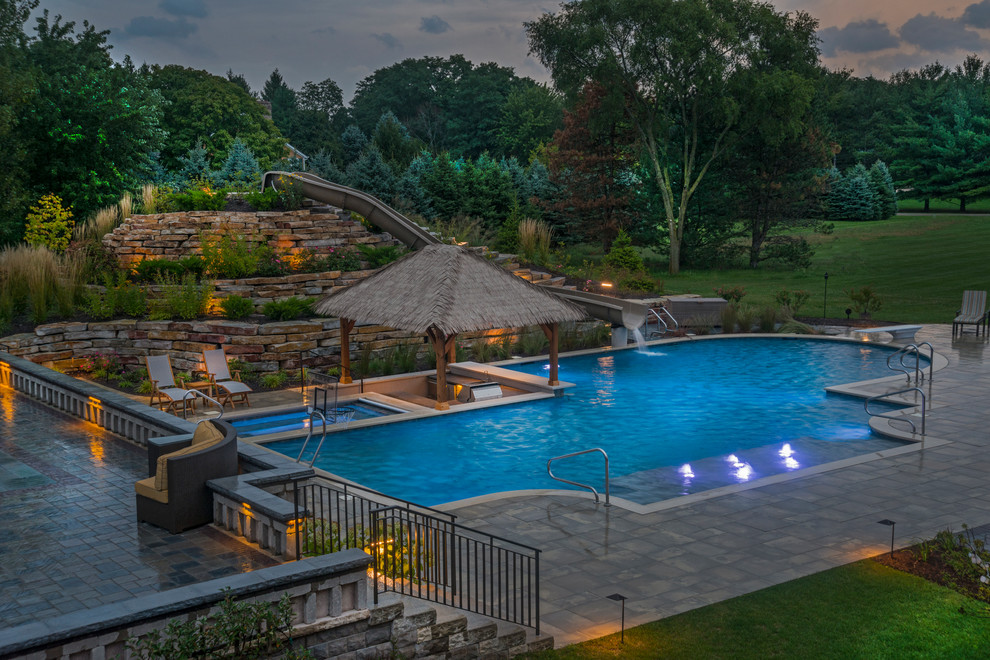 Expansive world-inspired back custom shaped lengths swimming pool in Chicago with a water slide and natural stone paving.