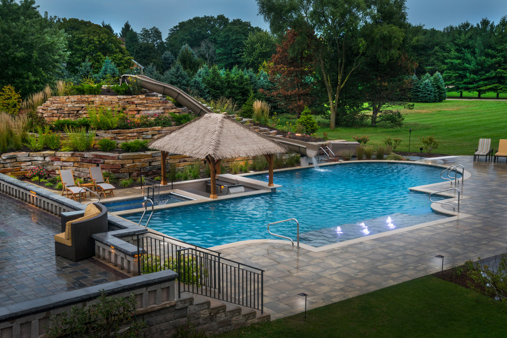 Diseño de piscina con tobogán alargada tropical extra grande a medida en patio trasero con adoquines de piedra natural