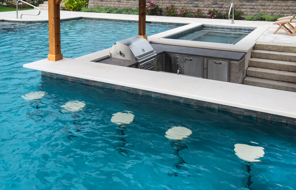 Idee per un'ampia piscina monocorsia tropicale personalizzata dietro casa con pavimentazioni in pietra naturale e una vasca idromassaggio