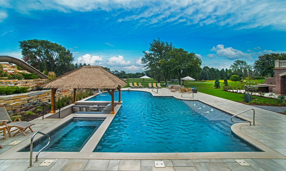 Foto de piscina con tobogán alargada tropical extra grande a medida en patio trasero con adoquines de piedra natural