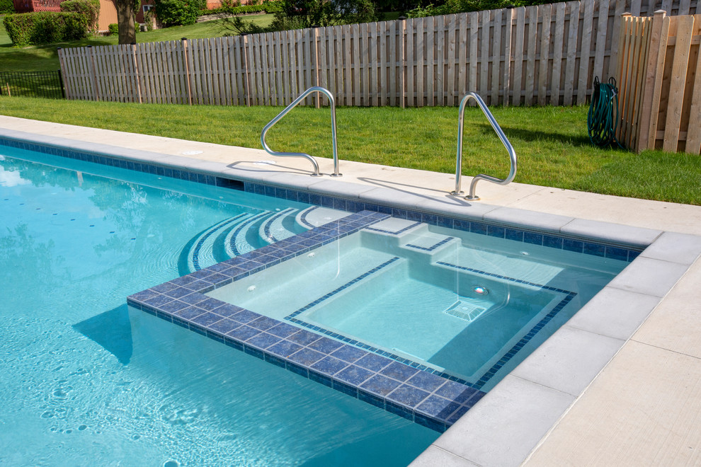 Esempio di una piscina monocorsia chic rettangolare di medie dimensioni e dietro casa con una vasca idromassaggio e lastre di cemento