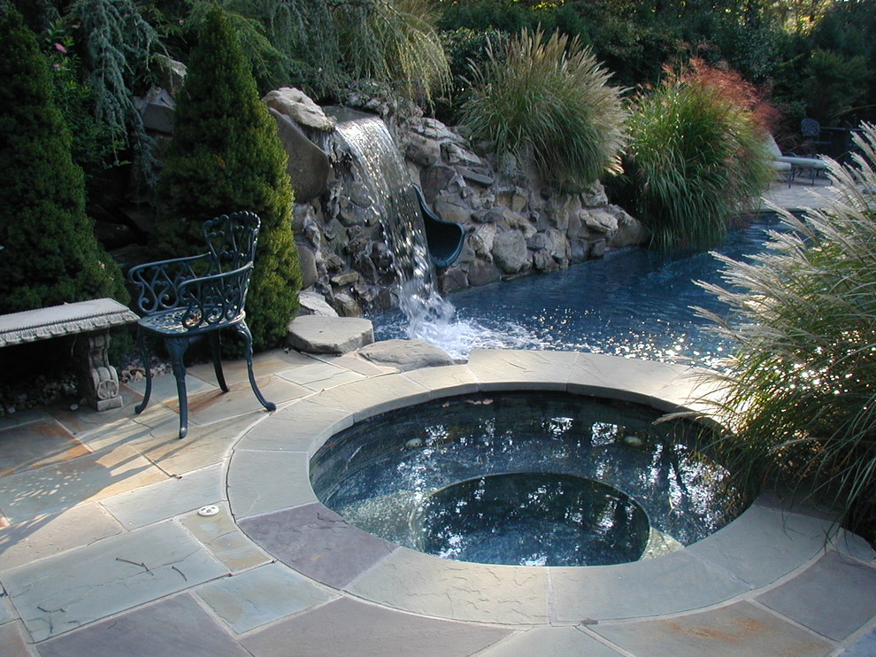 Aménagement d'une grande piscine naturelle et arrière classique ronde avec un point d'eau et des pavés en pierre naturelle.
