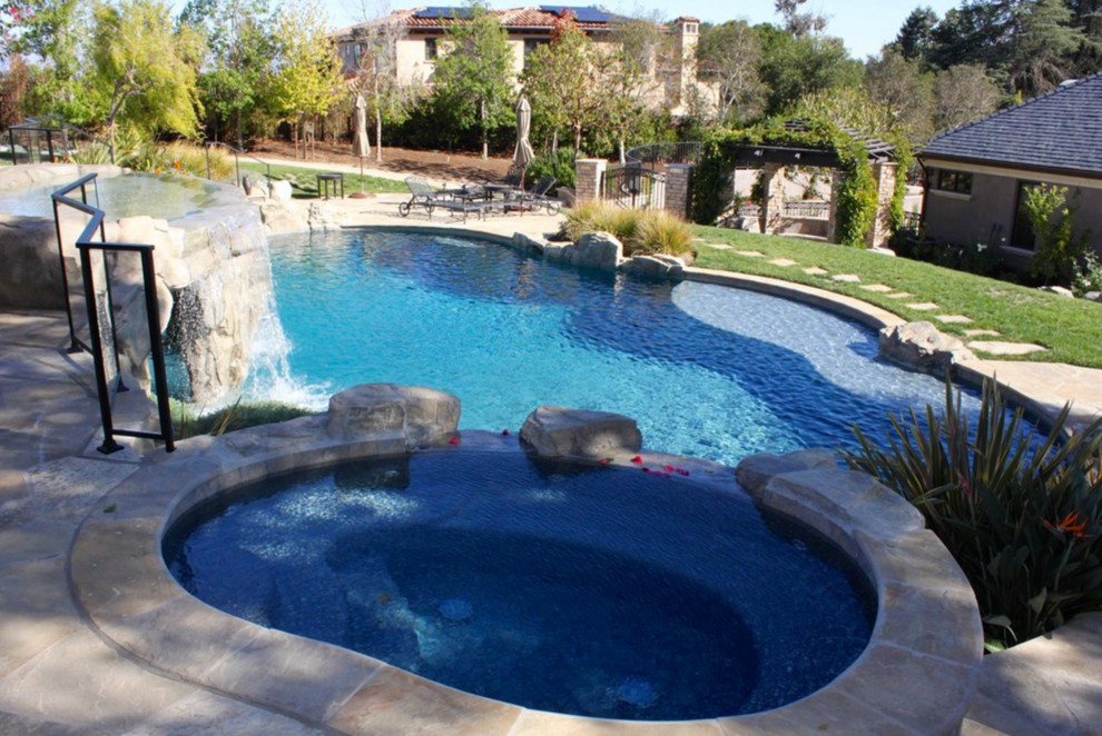Immagine di una grande piscina naturale mediterranea personalizzata dietro casa con fontane e pavimentazioni in pietra naturale
