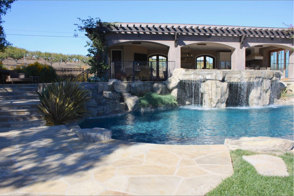 Diseño de piscina con fuente natural mediterránea grande a medida en patio trasero con adoquines de piedra natural