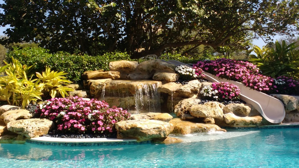 Modelo de piscina con tobogán infinita costera grande rectangular en patio trasero con adoquines de piedra natural