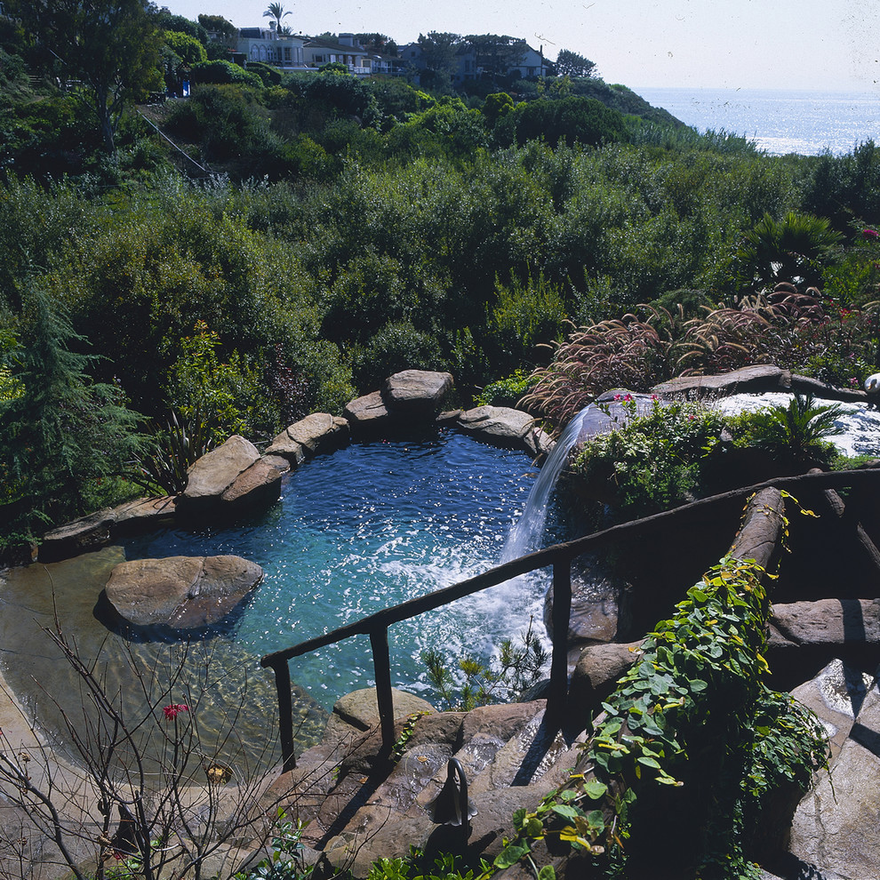 World-inspired back custom shaped swimming pool in Los Angeles with a water feature and natural stone paving.