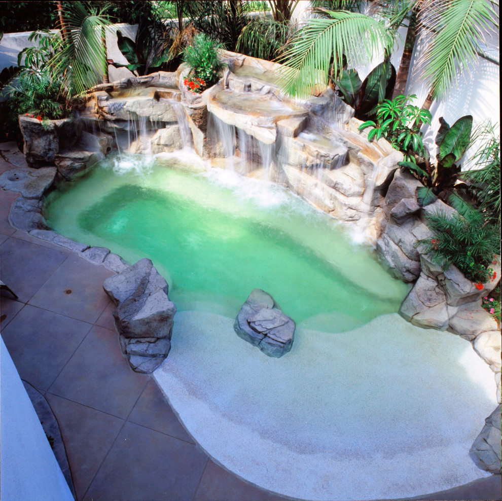 Design ideas for a world-inspired back custom shaped swimming pool in Los Angeles with a water feature and natural stone paving.