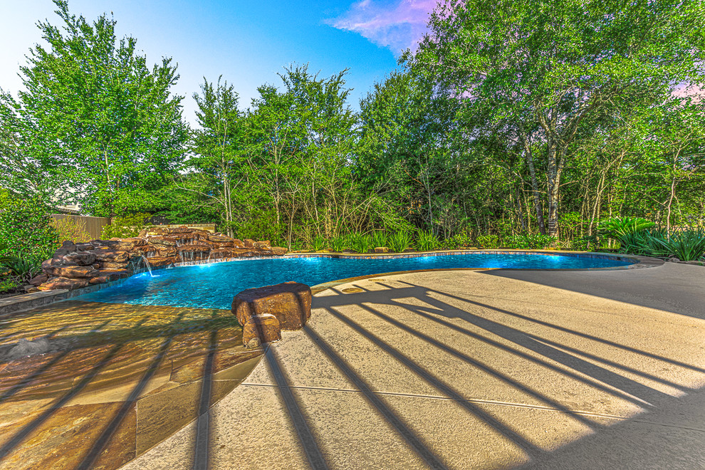 Imagen de piscina natural exótica grande a medida en patio lateral con losas de hormigón