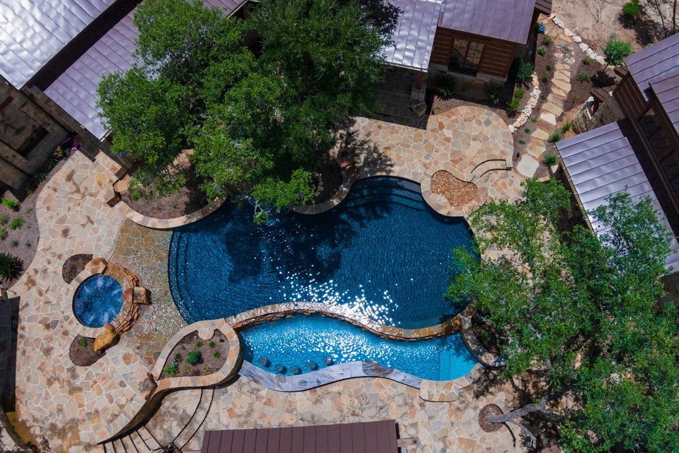 Large rustic back custom shaped infinity hot tub in Austin with natural stone paving.