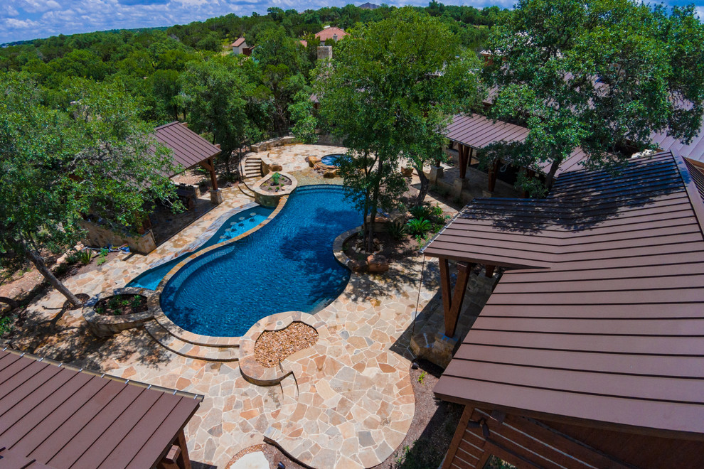 Example of a large mountain style backyard stone and custom-shaped infinity hot tub design in Austin