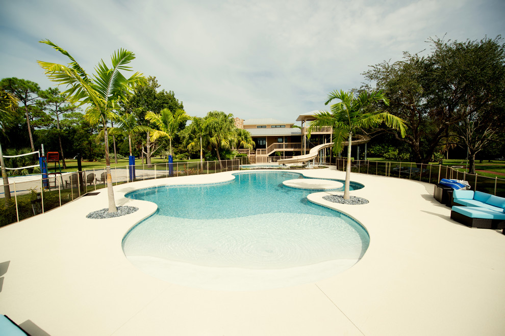 Huge beach style backyard custom-shaped natural pool photo in Miami with decking