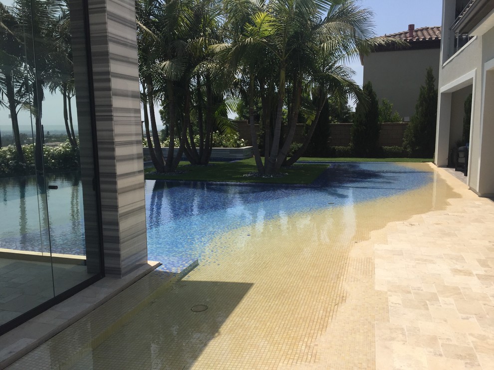This is an example of a large beach style back custom shaped swimming pool in Orange County with a water feature and tiled flooring.