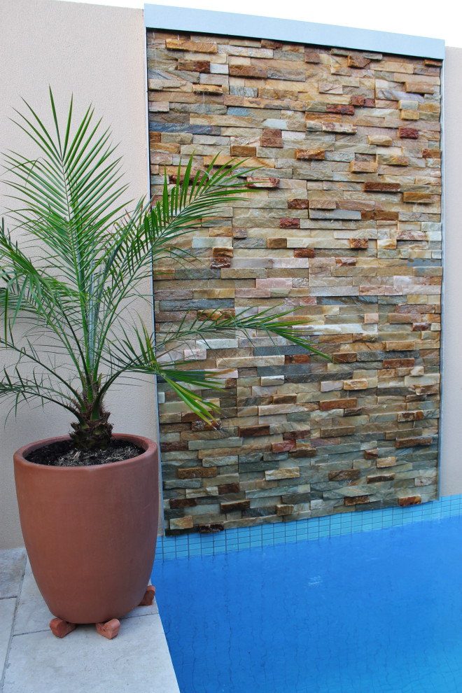 Diseño de piscina con fuente alargada actual de tamaño medio rectangular en patio trasero con adoquines de piedra natural