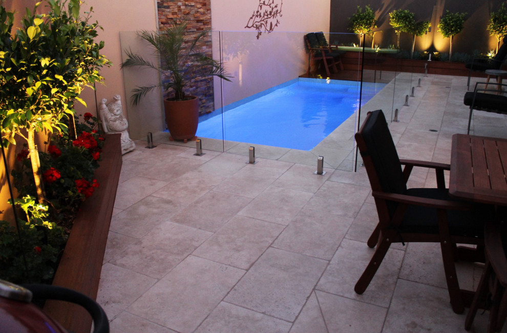 Modelo de piscina con fuente alargada actual de tamaño medio rectangular en patio trasero con adoquines de piedra natural