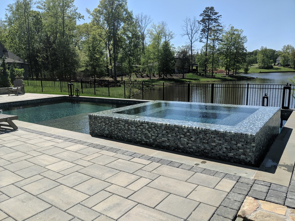 Cette image montre une piscine à débordement et arrière design de taille moyenne et rectangle avec un bain bouillonnant et des pavés en béton.