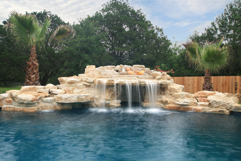 Large rustic back custom shaped natural swimming pool in Austin with a water feature and decking.
