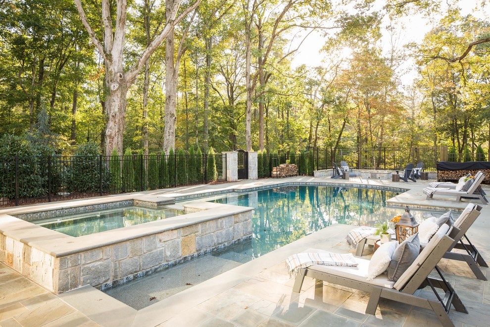 This is an example of a large rural back l-shaped swimming pool in Atlanta with natural stone paving and fencing.