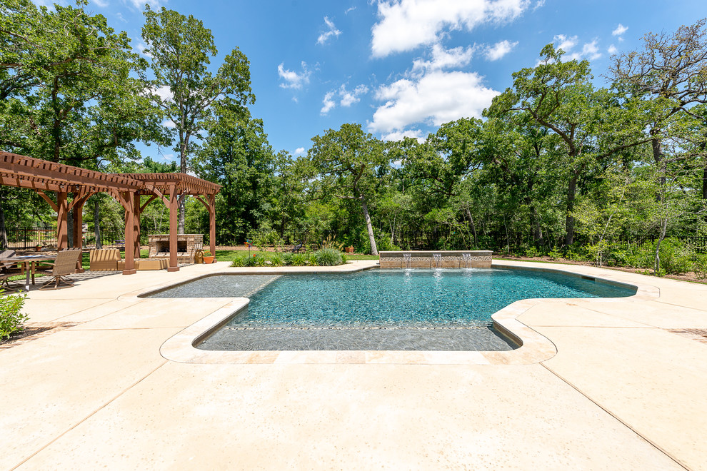 Ejemplo de piscina natural grande a medida en patio trasero con suelo de hormigón estampado