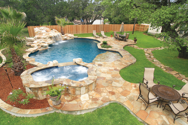 This is an example of a large rustic back custom shaped natural swimming pool in Austin with a water feature and decking.