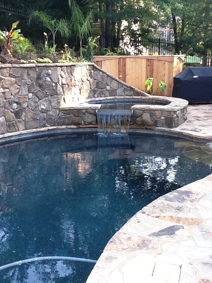 Immagine di una piscina naturale chic a "C" di medie dimensioni e dietro casa con una vasca idromassaggio e pavimentazioni in pietra naturale