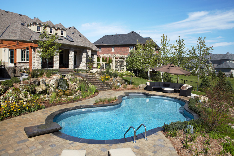Inspiration for a large traditional back custom shaped natural swimming pool in Toronto with a water feature and brick paving.