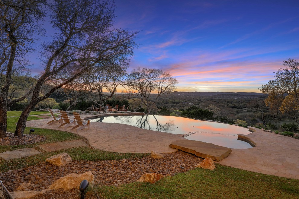 This is an example of a rural back custom shaped infinity hot tub in Austin with natural stone paving.