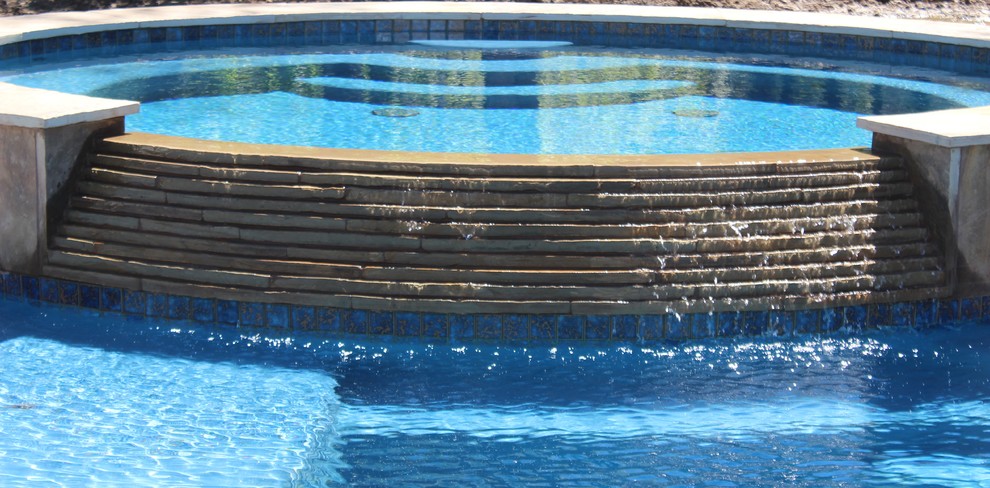 На фото: большой естественный, круглый бассейн на заднем дворе в морском стиле с джакузи и мощением тротуарной плиткой с