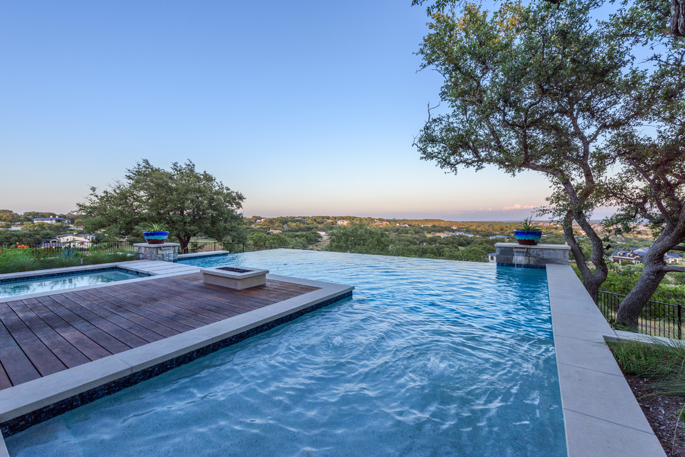 Immagine di una piscina a sfioro infinito design a "L" di medie dimensioni e dietro casa con una vasca idromassaggio e pavimentazioni in pietra naturale