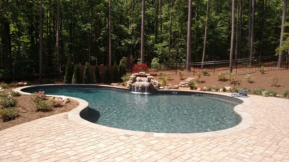 Modelo de piscina con fuente natural clásica renovada grande a medida en patio trasero con adoquines de ladrillo