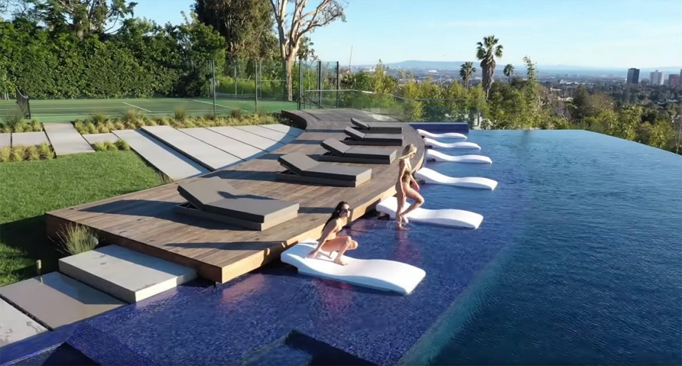 Expansive contemporary back custom shaped infinity swimming pool in Los Angeles with a water feature and decking.