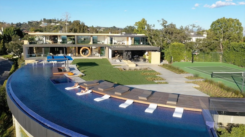 Immagine di un'ampia piscina a sfioro infinito design personalizzata dietro casa con fontane e pedane
