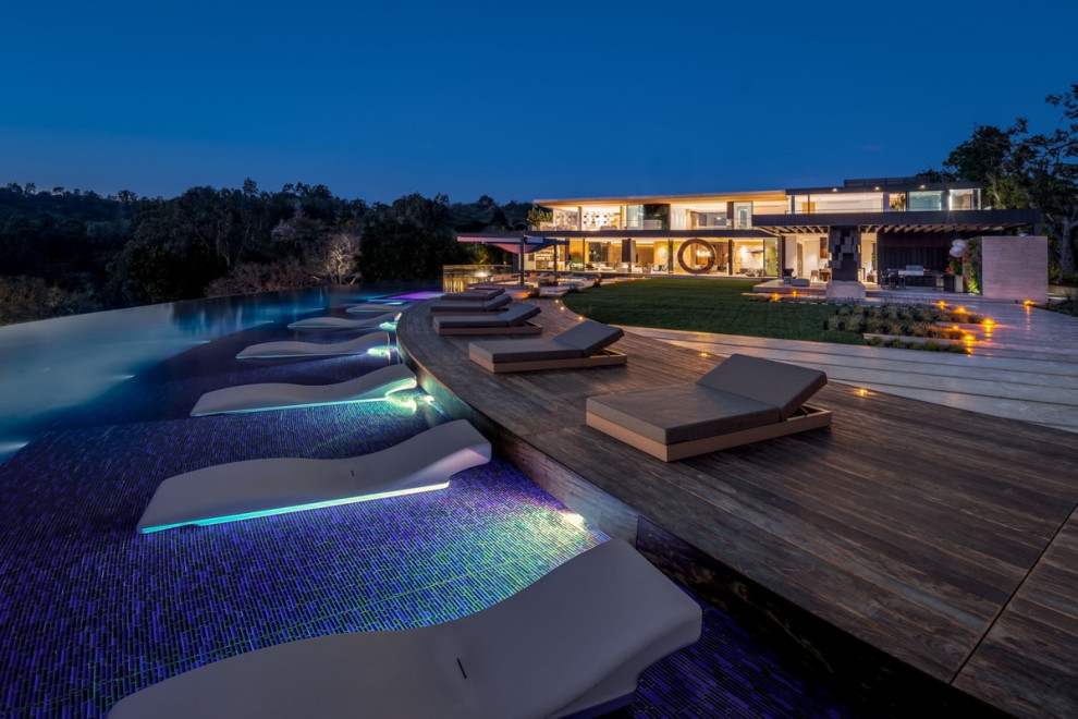 Esempio di un'ampia piscina a sfioro infinito design personalizzata dietro casa con fontane e pedane
