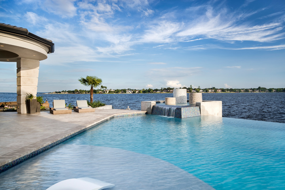 Immagine di un'ampia piscina a sfioro infinito stile marino personalizzata dietro casa con fontane