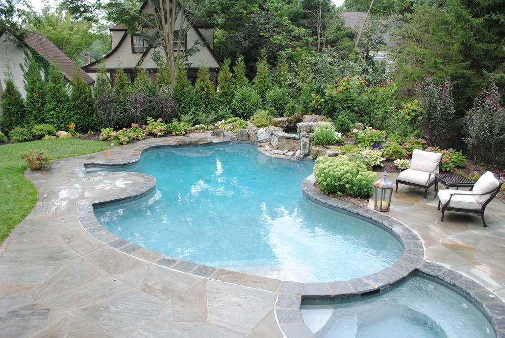 Klassisk inredning av en stor njurformad pool på baksidan av huset, med spabad och naturstensplattor