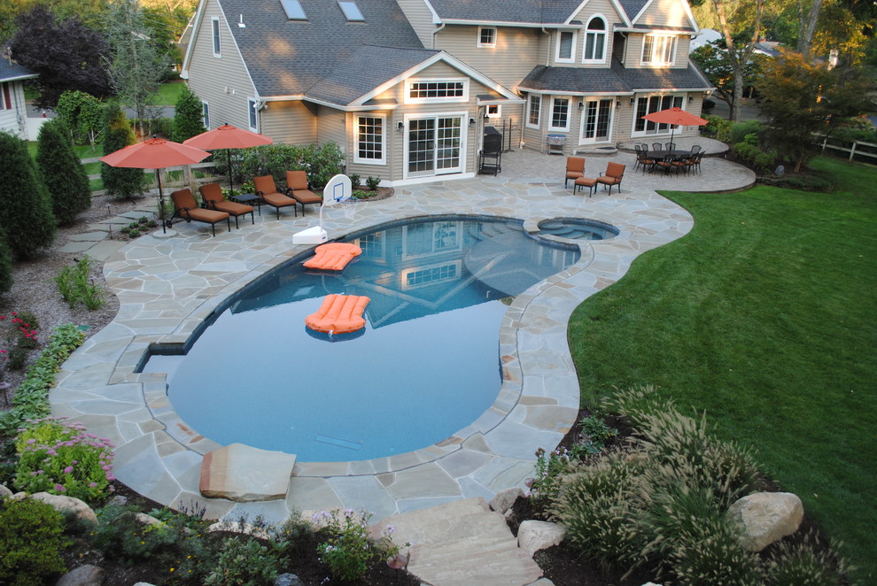 Idée de décoration pour une grande piscine arrière tradition en forme de haricot avec un bain bouillonnant et des pavés en pierre naturelle.