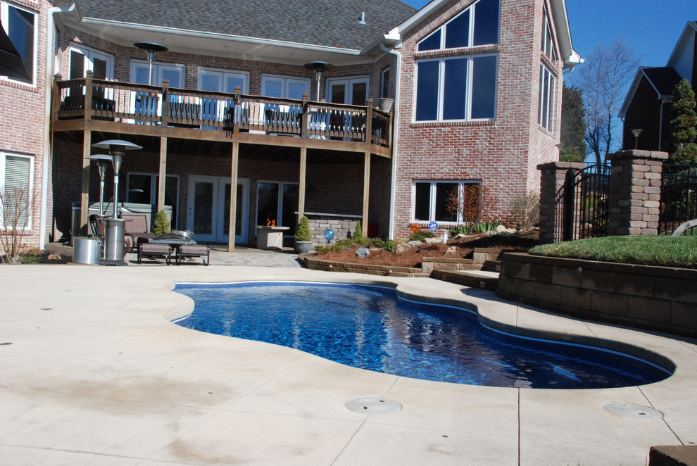 Modelo de piscina actual de tamaño medio a medida en patio trasero con adoquines de hormigón