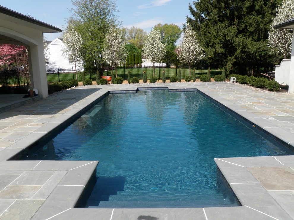 Ejemplo de piscina con fuente alargada clásica rectangular en patio trasero con adoquines de piedra natural