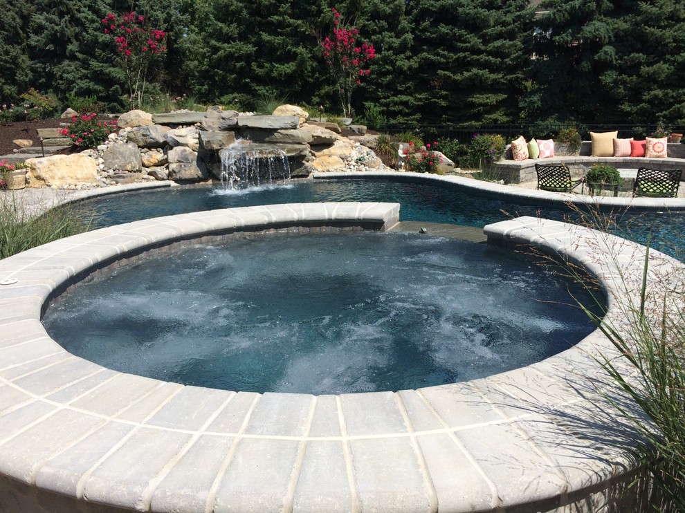 Modelo de piscina natural clásica grande a medida en patio trasero con adoquines de hormigón