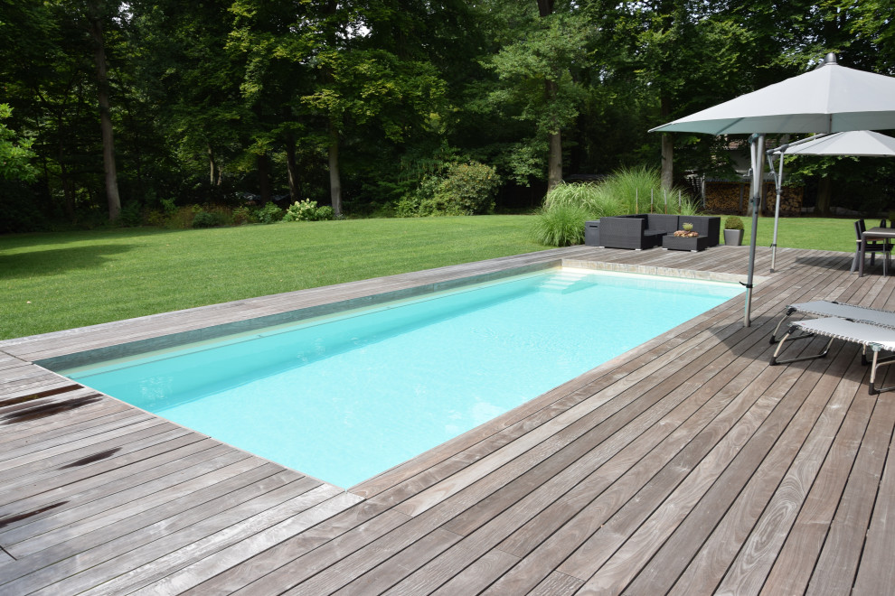 Réalisation d'une grande piscine latérale tradition rectangle avec une terrasse en bois.