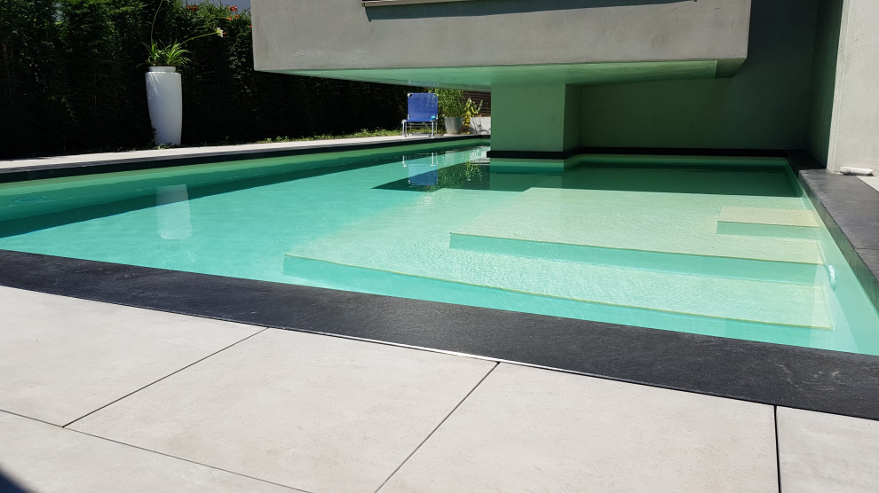 Imagen de piscina actual grande a medida en patio lateral con adoquines de piedra natural