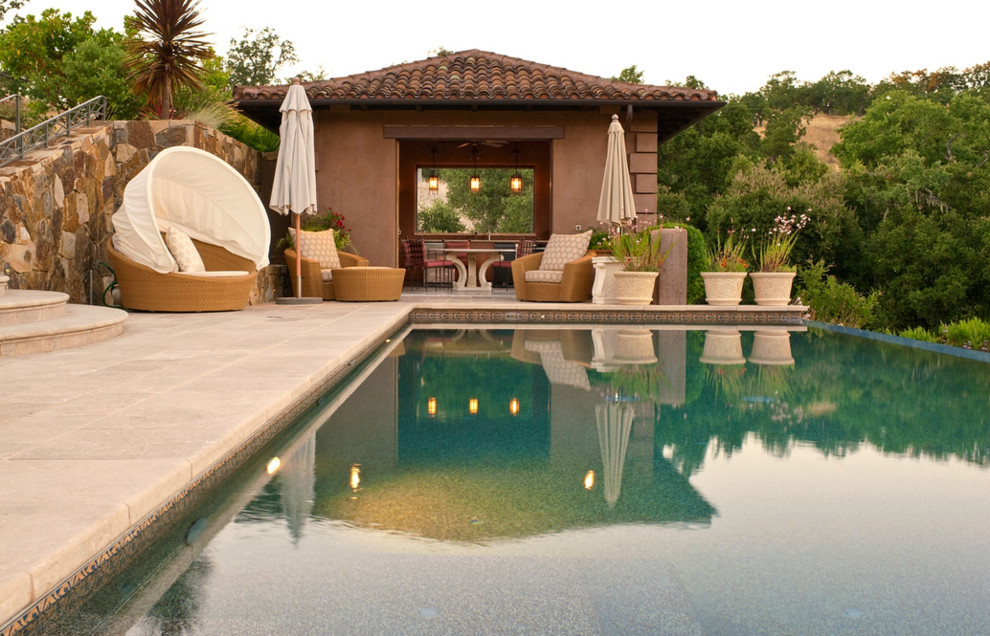 На фото: большой прямоугольный бассейн-инфинити на заднем дворе в средиземноморском стиле с покрытием из каменной брусчатки с