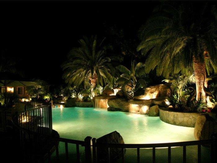 Idee per una grande piscina tropicale personalizzata dietro casa con fontane e pavimentazioni in pietra naturale