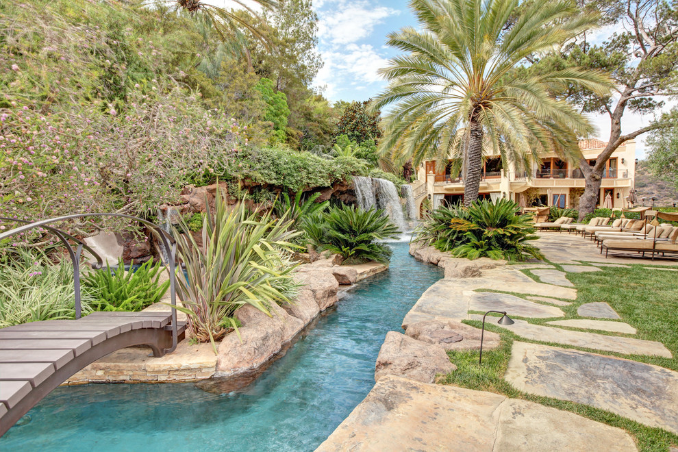 Ejemplo de piscina con tobogán natural tropical extra grande a medida en patio trasero con adoquines de piedra natural